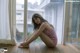 A woman sitting on a wooden floor in front of a window.