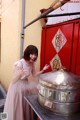 A woman in a pink dress standing next to a large metal pot.