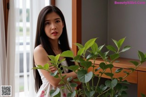 A woman standing next to a plant in front of a window.