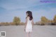 A woman in a white dress standing on a dirt road.